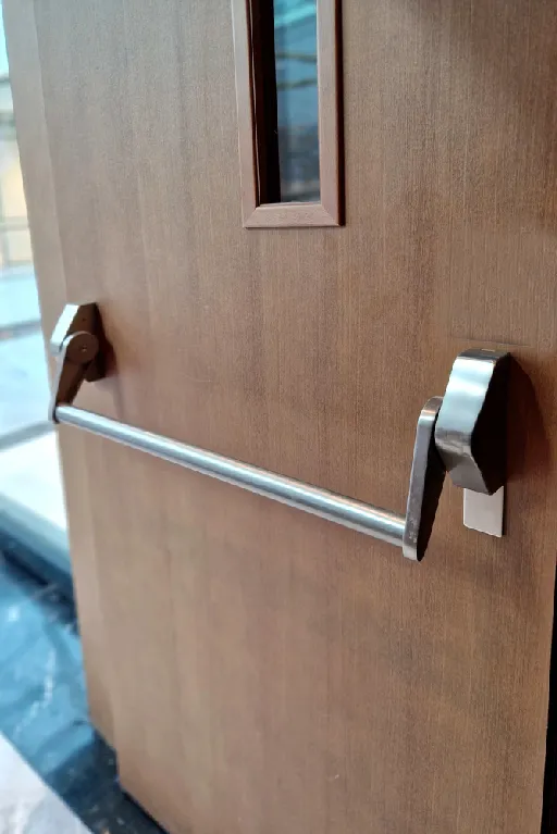 Wood commercial door with stainless-steel push bar exit device, professionally installed for safe, code-compliant egress in Melbourne and Orlando, FL.