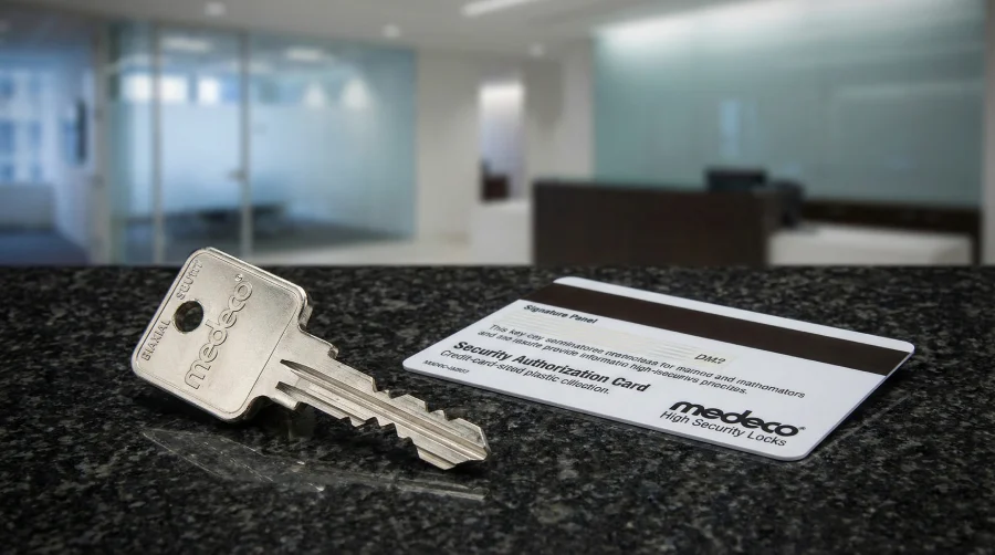 Close-up of a Medeco high-security key and restricted duplication authorization card on a counter, illustrating total key control systems installed by Sunshine Mobile Locksmith for businesses in Melbourne, FL.